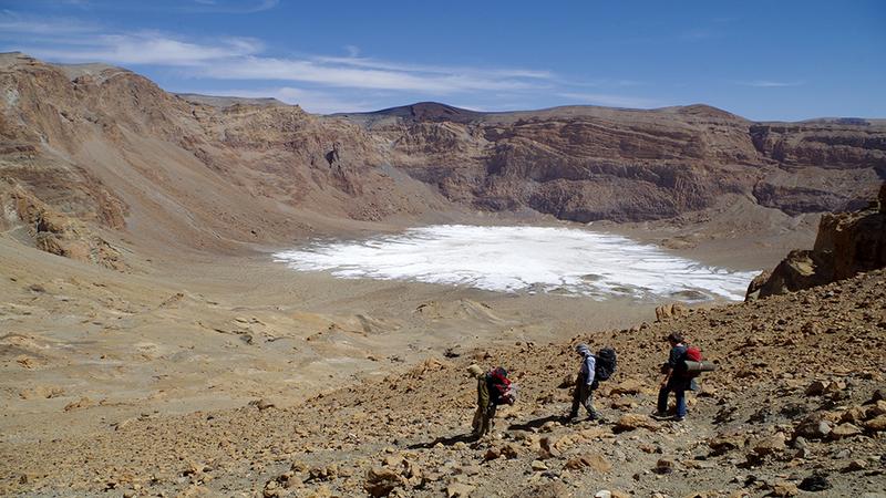 Abstieg in den Era-Kohor-Subkrater innerhalb der Gipfelcaldera des Emi Koussi - mit 3415 m der höchste Berg der Sahara. Auf dem Kraterboden liegen weißliche Sedimente: evaporitische Salzkrusten, Reste eines Paläosees, der den Krater teilweise füllte.