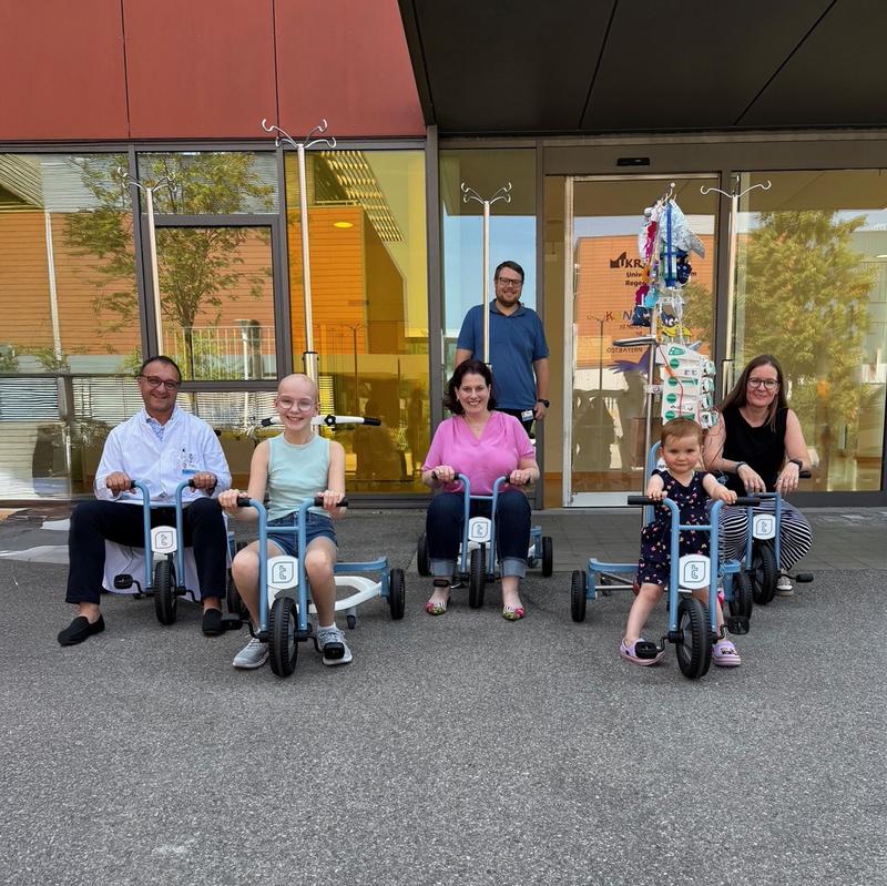 Sabine Lange (Kaufmännische Direktorin, Mitte) übergibt die Dreiräder für die Kinder der PHOS-Stationen an Prof. Dr. Selim Corbacioglu (Direktor der Abteilung für Pädiatrische Hämatologie, Onkologie und Stammzelltransplantation, li.).