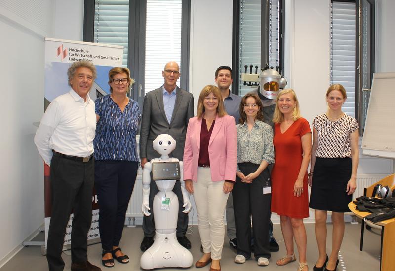 Staatssekretärin Nicole Steingaß (MWG RLP) rechts neben Roboter ‚Pepper‘ zusammen mit dem Projektteam und der Hochschulleitung 
