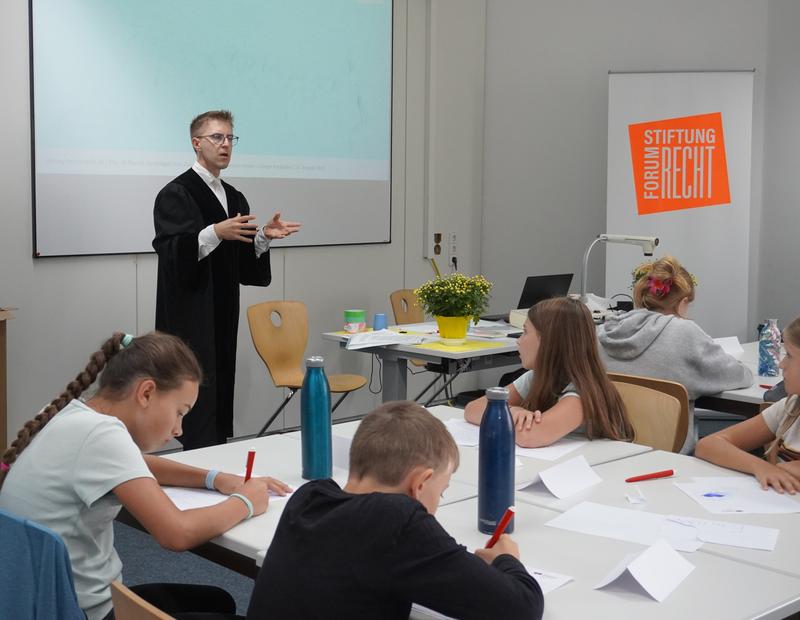 Ein Richter des Landgerichts Karlsruhe erklärt den jungen Teilnehmern des SommerKinderCollege 2025 die Abläufe und die Bedeutung der Arbeit bei Gericht.