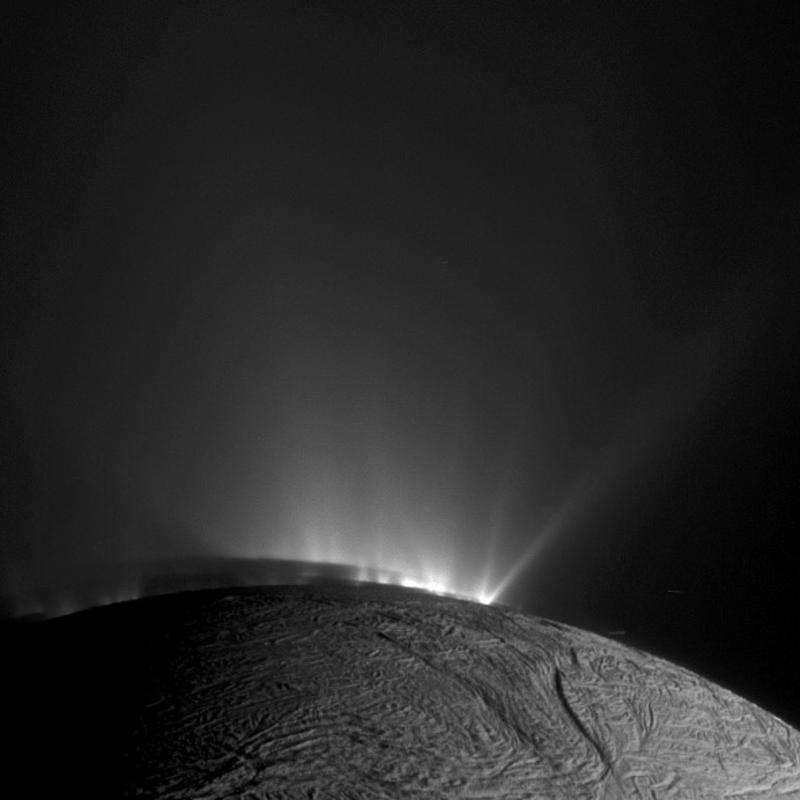 Blick über den Südpol des eisigen Saturnmondes Enceladus: Aus Rissen in der eisigen Oberfläche des Mondes, die als „Tigerstreifen” bekannt sind, spritzt Material heraus. Enceladus Schatten ist deutlich auf den unteren Teilen der Fontänen zu sehen. 