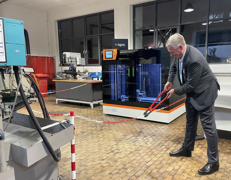 Prof. Dr. Küstermann schneidet feierlich das Band zur Inbetriebnahme des neuen großformatigen 3D-Druckers durch. Bildrechte: DHBW KA//S. Wagner
