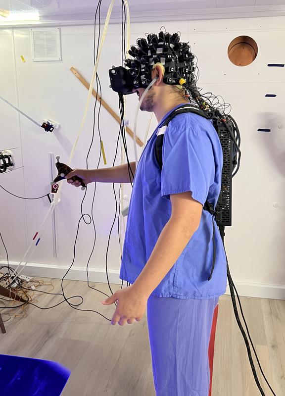Das Bild zeigt eine Hilfskraft von Prof. Dominik Bachs Team am University College London mit Messhelm und dem Prototyp der neuen OPMEG-kompatiblen VR-Brille. 