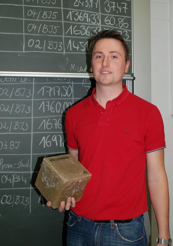 Alexander Neumann mit seinem Epoxidharzbeton-Würfel vor der Ergebnistafel im Betonprüflabor der HTWK Leipzig.