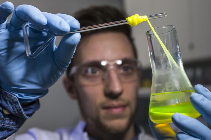 Ein Mitarbeiter zieht im Labor für Systembiotechnologie an der Universität des Saarlandes einen Bionylonfaden aus einem Glaskolben. 