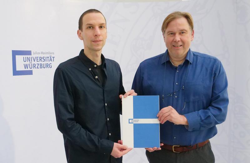 JMU-Vizepräsident Matthias Bode (rechts) überreicht Prof. Dr. Jonas Czwikla die Ernennungsurkunde zur W2-Professur für Versorgungsforschung an der Universität Würzburg. 