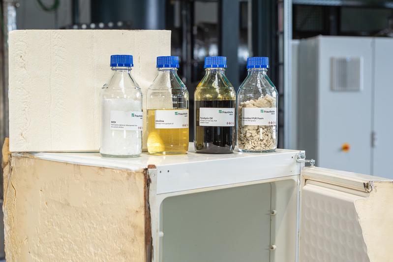 Aus Hartschaum-Abfällen (rechts) wird ein Pyrolyseöl (2. von rechts) erzeugt. Hieraus wird Anilin in großer Reinheit extrahiert (3. von rechts), welches als Rohstoff für MDI eingesetzt wird. MDI ist der wichtigste Rohstoff für Polyurethan-Schäume. 