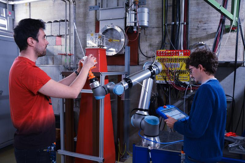Postdoc Dr. Enrico Pierobon (l.) und Doktorand Luca Lunati aus der GSI/FAIR-Biophysik befestigen ein Mikrodosimeter an einem Roboterarm.