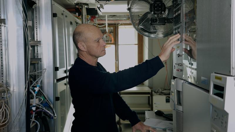 Empa‑Forscher Stefan Reimann auf dem Jungfraujoch vor dem «Medusa»-Messsystem, einem speziell für das AGAGE‑Netzwerk entwickelten Gaschromatograph‑Massenspektrometer, das zahlreiche Spurengase in der Atmosphäre automatisch misst.