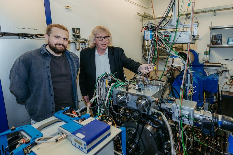 Aristidis Dafis und Prof. Rottengruber (von links nach rechts) vom Institut für Engineering von Produkten und Systemen mit einem 1-Zylinder Versuchsmotor am Motorenprüfstand auf dem Campus der Uni Magdeburg. 