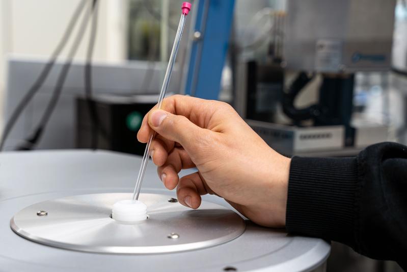 Eine chemische Probe in einem Glasröhrchen wird in ein NMR-Spektrometer geführt.