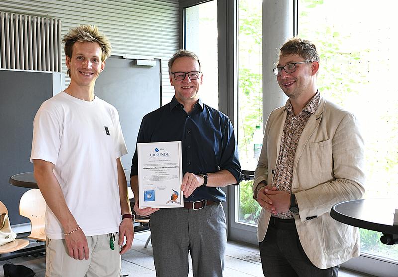 Prof. Dr. Christoph Skornia (Mitte), Vizepräsident für Nachhaltigkeit und Digitalisierung, und Lenz Franzke (l.), Leiter des Green Office der OTH Regensburg, nehmen die Auszeichnung „Vogelfreundliches Glas“ von Dr. Peter Stimmler (r.) vom LBV entgegen.