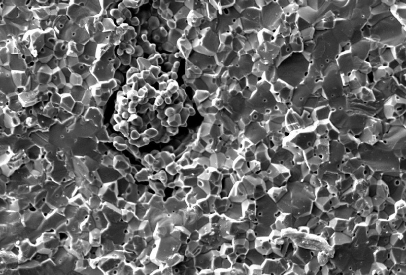 Bruchauslösender Defekt in Aluminiumoxid, der durch eine beim Verpressen ungenügend zerstörte Granalie entstanden ist. Der ringförmige Spalt um die "himbeerartige" Sturktur hat einen Druchmessser von ca. 50 Mikrometer.