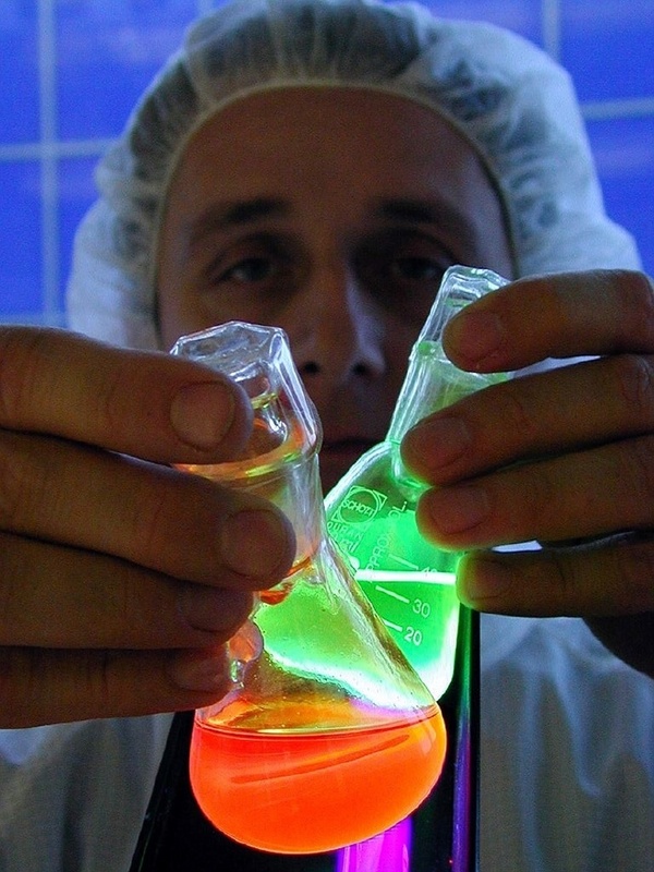 Dr. Wedel zeigt Lösungen der Polymere, die hier unter einer UV-Lampe in unterschiedlichen Farben leuchten.