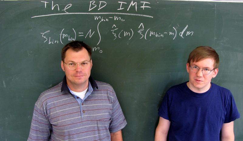 Prof. Pavel Kroupa (links) und Ingo Thies vor der Formel, die die Masseverteilung von Paaren Brauner Zwerge beschreibt