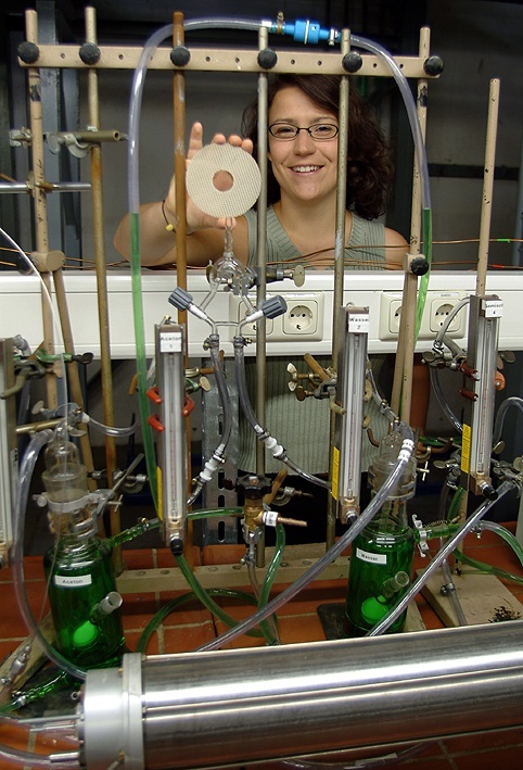 Dr. Meyer hält ein mit Titandioxid beschichtetes Aluminiumnetz in der Hand, dessen geruchstötenden Eigenschaften in der Versuchsanlage vor ihr getestet werden. (Foto: Cott/FSU-Fotozentrum)