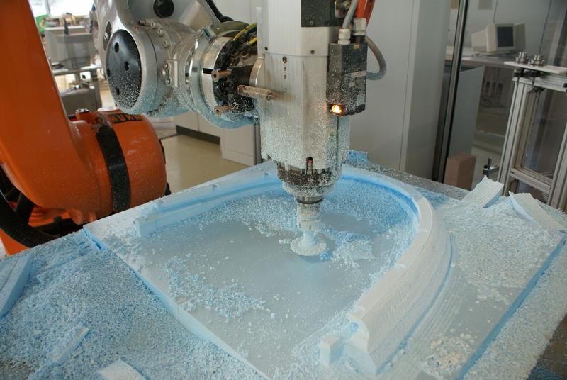 Ein Industrieroboter fräst eine Gussform für ein großes Bauteil.