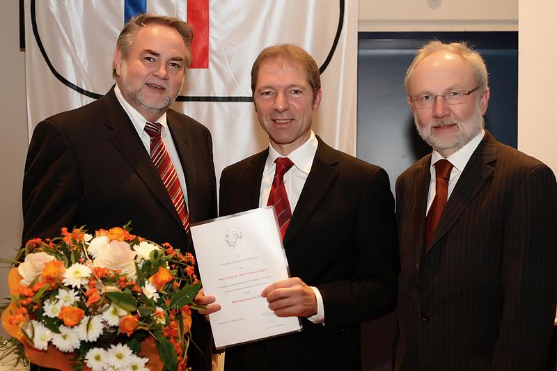 Prof. Dr. Volker Nienhaus, Präsident der Philipps-Universität Marburg (li.) und Prof. Dr. Heinz-Josef Schmitt, Head Global Medical Affairs Novartis Behring (re.), gratulieren dem Behring Lecture-Preisträger Prof. Dr. Ralf Bartschlager (mitte).  