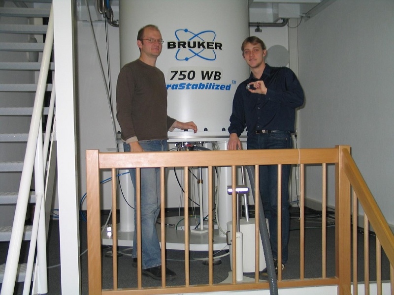 Dr. Daniel Huster (l.) und Ronny Schulz (Arbeitsgruppe Prof. Bader) mit einem Prototyp des Bioreaktors vor dem 750-MHz-NMR-Spektrometer