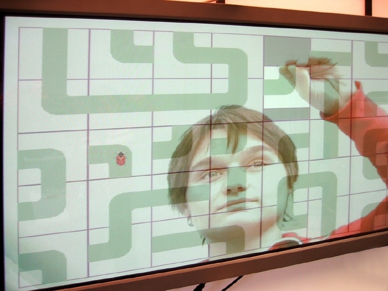 Das Bild der Spielerin wird elektronisch mit dem Spiel gemischt. Verschiebt sie die virtuellen Steine günstig, hat der Käfer im Irrgarten freie Bahn. © Fraunhofer IIS