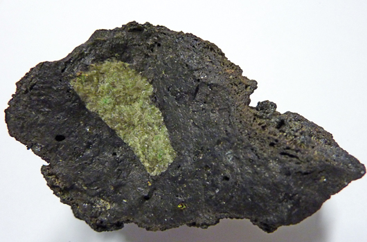 Typisches Beispiel eines Basalts (schwarz) mit Xenolith (grün).